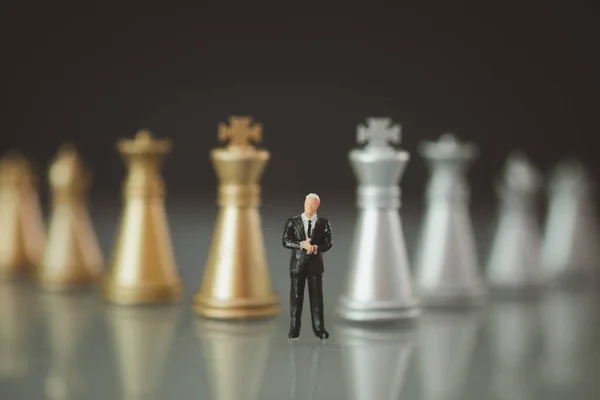 Business and competition concept. Businessman miniature figure standing in front of golden and silver chess pieces. Target and decision concept