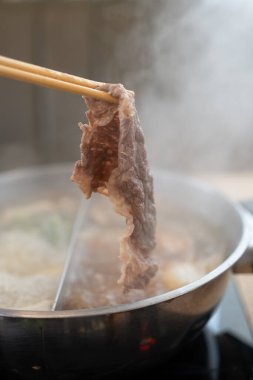 Adam ender bulunan Wagyu 'yu kaynayan bir Shabu tenceresinden dumanla yakalamak için çubuk kullanıyordu. Popüler yiyecekler parça parça pişirilir.