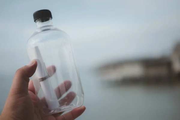 Message in a bottle in hand on blue sky background. Mysterious message