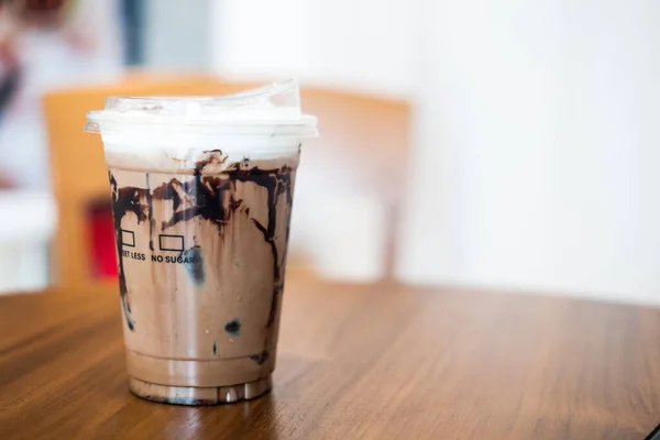Iced mocha, coffee and cocoa powder mixed with sweetened condensed milk and fresh milk top with soft milk froth and cocoa powder in a takeaway plastic glass, showing texture of chocolate sauce