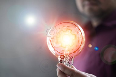 İnsan eli ampulü tutuyor ve yeni teknoloji icadı, yeni ilham, yenilik ve gelişim için bir vites simgesi var. Yeni iş fikri kavramı