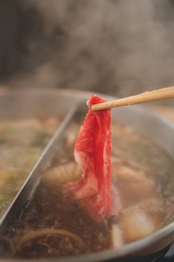 Sukiyaki tenceresine taze et getirmek için çubuk kullanmak. Japon shabu-shabu veya Sukiyaki.