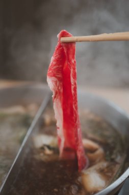 Çubuklar taze etli shabu-shabu ile sıcak çorbayı karıştırıyor. Japon shabu-shabu veya Sukiyaki.