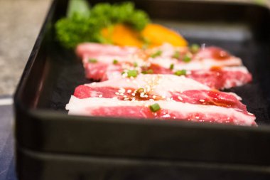 Izgara için taze çiğ domuz eti dilimi susam tohumları ve siyah tepside servis edilen taze soğan.