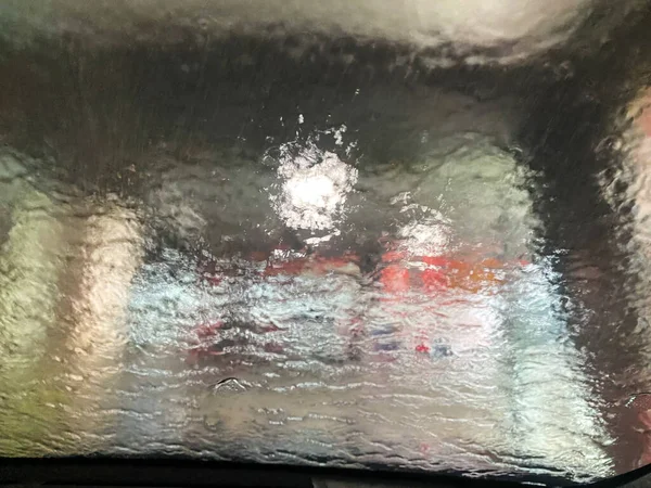 Drive view looking out through the windshield while going through an indoor automatic car wash, foam, bubbles and water on the windshield
