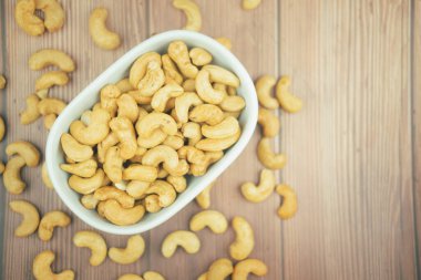 Roasted cashew nuts in white bowl on wood background.
