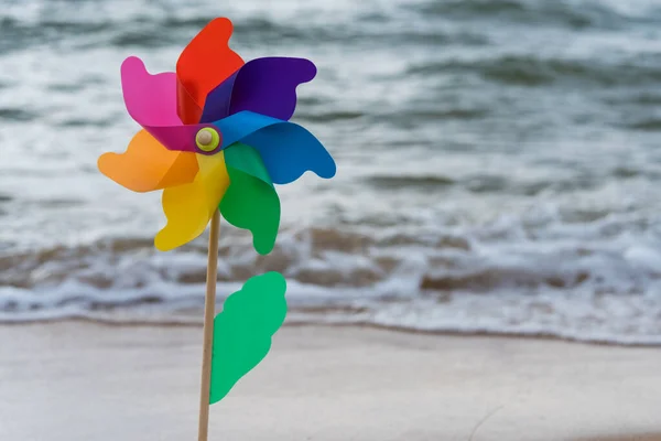 Bright toy colorful windmill decoration in the beach with wave background. Summer beach holiday background