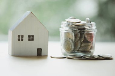 Full of Thai currency coin in saving jar with wood home on table with nature background. Real estate investment, property investment, plan for housing concept.