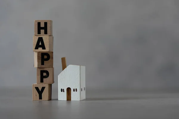 Wooden blocks with the text words HAPPY with a white wood home model. The concept of housing a young family, happy in home