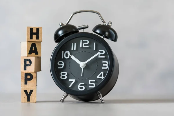 The concept of happy relaxing time. Happy on wood cube block and black clock. Free time management concept, creative idea, minimal concept.