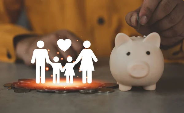Coins and the paper cut of family with hand of man put coin into piggy bank on wood table, Saving money for starting a married life, family planning concept, fundraising, superannuation concept.