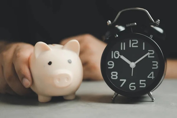 Hand holding a piggy bank and alarm clock. The concept for saving time. Saving time investment budget wealth business retirement, financial, money, banking concept.
