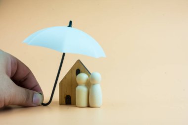 Tahta bebekler ve evler beyaz bir şemsiye altında tahta bebekleri ve evi koruyorlar, planlıyorlar, aileleri kurtarıyorlar, riskleri ve krizleri önlüyorlar ve sigorta kavramlarını koruyorlar..