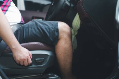 Man sets up a car driving position before driving on the road. Ergonomic expert adjustment of the driver's seat. Electric seat adjustment of car