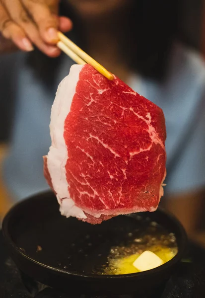 Close up of someone hand using chopsticks for cooking grilled beef over charcoal on stove in restaurant. Japanese style yakiniku food.