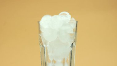 Sarı ışık arka planında yuvarlak buz küpleriyle boş bir bardağı döndürür.