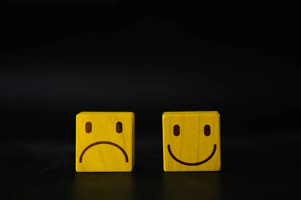 Choose between emotions in life, happy and sad, and choose the positive or negative. Emotion face symbol on yellow wooden cube blocks.