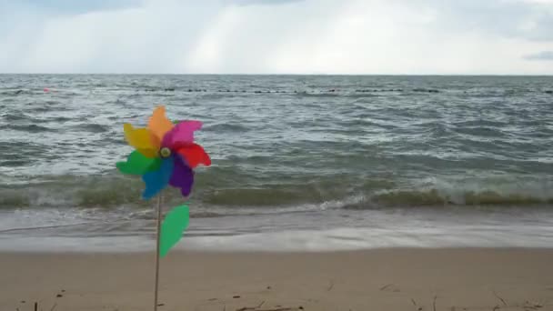在大海的蓝色光滑表面上 有一个旋转的带着一阵风的彩色塑料转轮站在沙滩上 — 图库视频影像