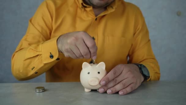 Ein Mann Gelben Hemd Steckt Münzen Ein Sparschwein Das Konzept — Stockvideo