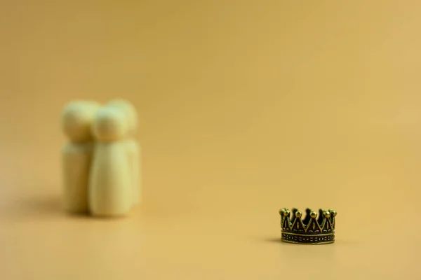 A crown with blur background of group wooden peg dolls. Human resources concept. Vacancy, worker getting promotion, recognition, and respect of colleagues. An employee with job promotion or success.