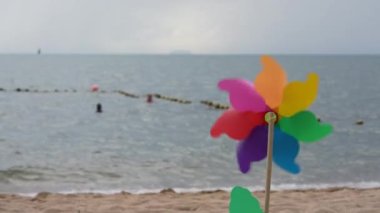 Plastik fırıldak, rüzgar esintisiyle renklenir. Denize karşı dalgalarla kum üzerinde durur. Uzayı kopyala Rahatla.