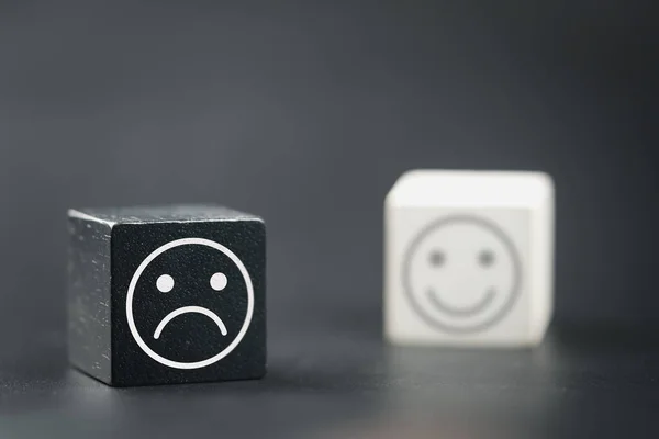 Wooden cube with an unhappy face, wood block with a emotion stress face and confused thoughts, depression and worry for distress and the smile face in white wood block of blur background