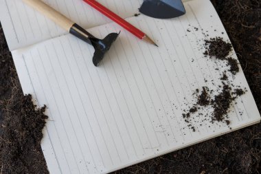 Üst görünüm boş defter, kalem ve kuru toprakta küçük bahçe aletleri. Üst görünüm