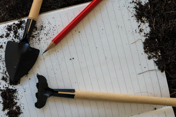 A notepad for writing, a pencil, gardening supplies, mini rakes, and shovels. Concept planting. Banner, top view photo. Close up.