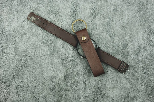 Leather key chain and leather wrist watch on a dark background. Top view