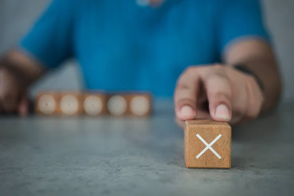 White cross mark, x, Wrong mark sign, Man showing a rejection sign in wooden cube. Concept of negative decision making or choice of vote with copy space for background or text.