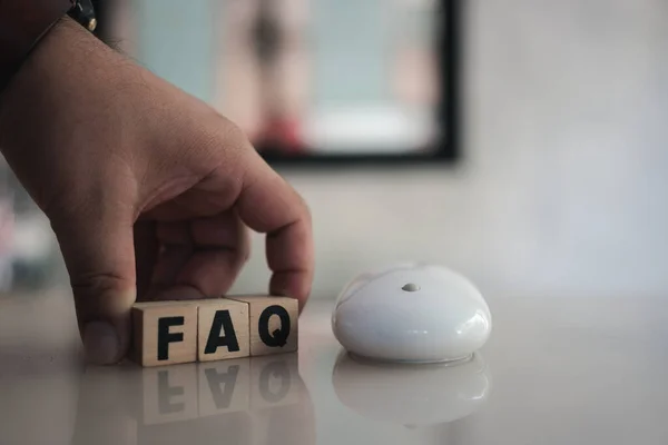 Wooden blocks with word FAQ with a computer mouse. FAQ abbreviation, frequently asked questions. Collection of frequently asked questions on any topic and answers to them. Instructions and rules