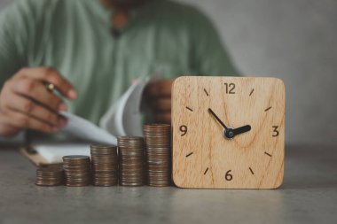 Girişimciler, iş sahipleri, muhasebeciler yatırım riskini değerlendirmek için ev bütçesini kontrol ediyorlar. Bozuk para ve tahta saatle yapılmış bir grafik. Zaman yönetimi kavramından para kazanmak