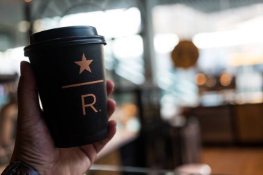 Samut Prakan, Tayland - 11 Temmuz 2023: Starbucks Rezerv sıcak kahve fincanı ve arka plan için bulanık Starbuck iç mekanı.