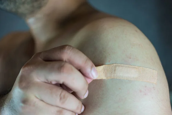 Man remove of a medical adhesive plaster to stick wound on shoulder. Cloe up