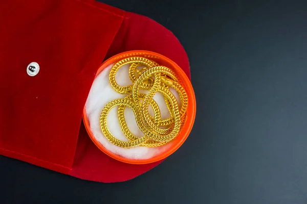 Gold necklace in a red box in the shape of a round with red velvet on a black background