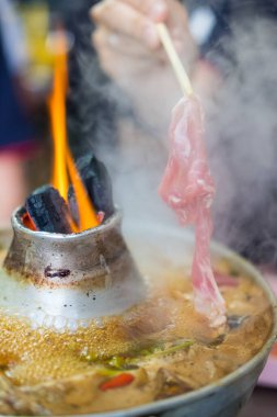 Tayland 'da popüler olan ve haşlanmış sığır eti, domuz eti, köfte ve sebzeyle birlikte pişirilmiş Tayland çorbası için ince domuz eti çubuğu kullanan bir adam..