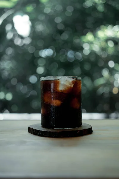 Cold brew coffee with ice on a wood table against nature background.