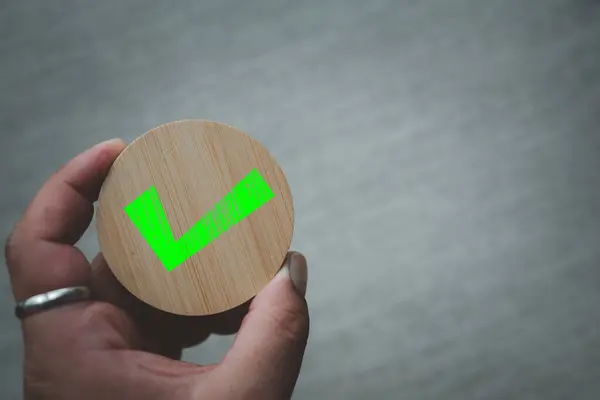 Close up green check mark icon on round wood, chosen green check mark by business\'s hand. Picking the correct sign and approving, voting or right decision concepts.