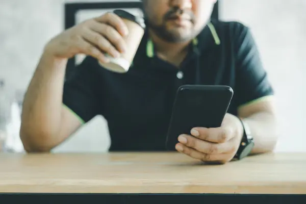 Casual man using mobile smartphone and holding a coffee cup in hand at coffee shop. Male hipsters using social network internet technology via mobile phone, modern people lifestyle concept