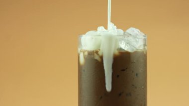 Buzlu kahveyle bardağa taze süt kreması döküyorum. Soğuk, ferahlatıcı yaz içeceği konsepti. Yavaş çekim ve döndürme