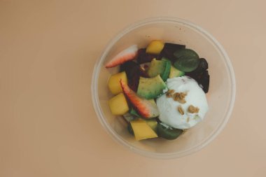 Taze meyve salatası ve yoğurt plastik bir kutuya konur. Meyve salatası çilek, üzüm, kivi ve mango gibi meyveler içerir.