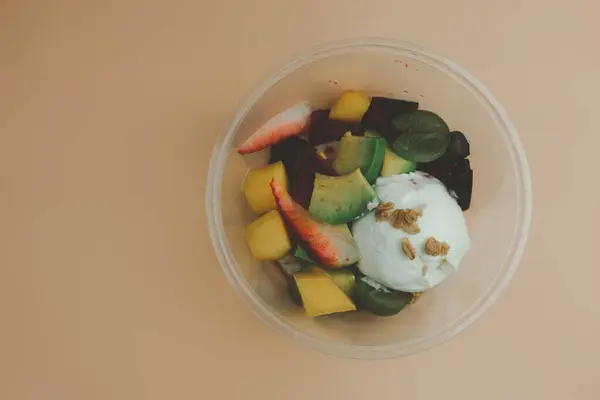 Fresh fruit salad and yogurt is placed in a box plastic container. The fruit salad contains fruit such as strawberries, grapes, kiwi and mango put fresh yogurt topping with peanuts