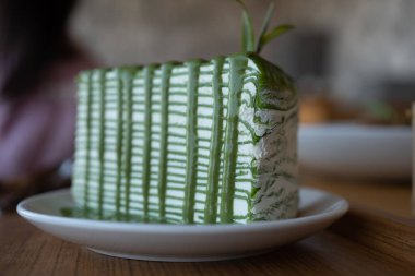 Yeşil çay soslu ve taze yeşil çay izinleriyle süslenmiş yeşil çay krepi kekini ahşap bir masanın üzerine koy.