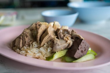 Tavuklu buğulanmış pirinç ve pembe tabakta salatalıklı sakatat.