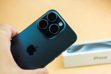 Bangkok, Tayland - 23 Ekim 2023: Mavi titanyum iPhone 15 Pro bir erkeğin elinde ve arka planında tutuluyor