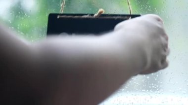 Dükkan sahibi kafenin ön kapısının kapanması ya da kapanması için vitrin levhasını kapatıyor, yağmurlu arka planda cam kapıdaki açık olan ahşap levhayı kapatıyor.