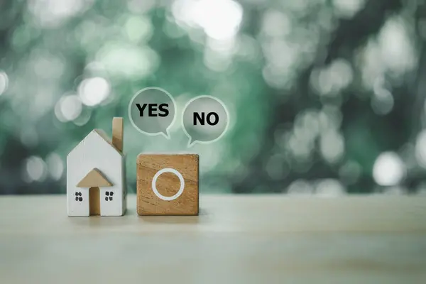A miniature home model with empty circles in wood block icons and Yes or No choice for making the decision. Decision making and choosing between right and wrong about buy home.