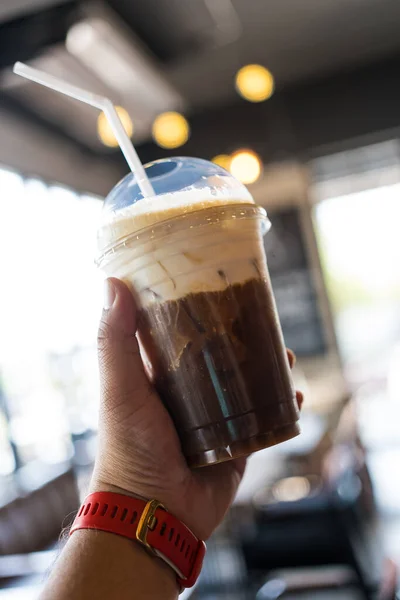 A glass of cold brew coffee topped with milk foam on blurred background in hand