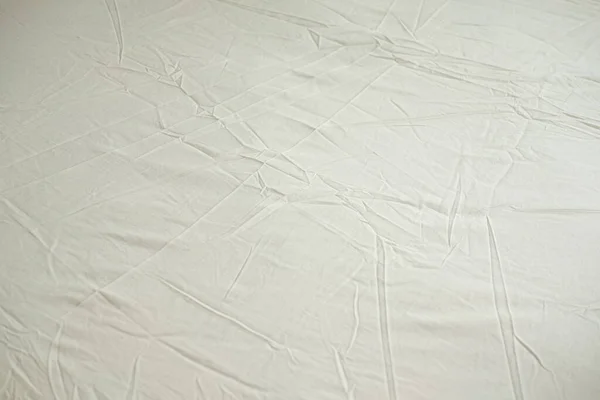 Crumpled bed sheet background texture. Light yellow fabric top view, light fabric
