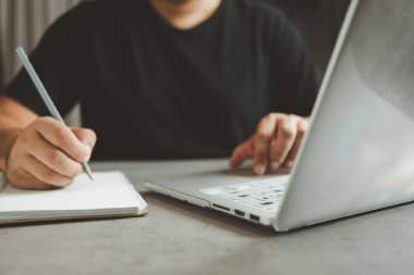 Belge üzerine bilgi yazan ve bir monitörden siparişi kontrol eden bir adam, küçük işletme ve perakende işinde serbest çalışan bir adam. İnternet mağazası siparişi alıyorum. Çevrimiçi kavram fikirleri satılıyor.
